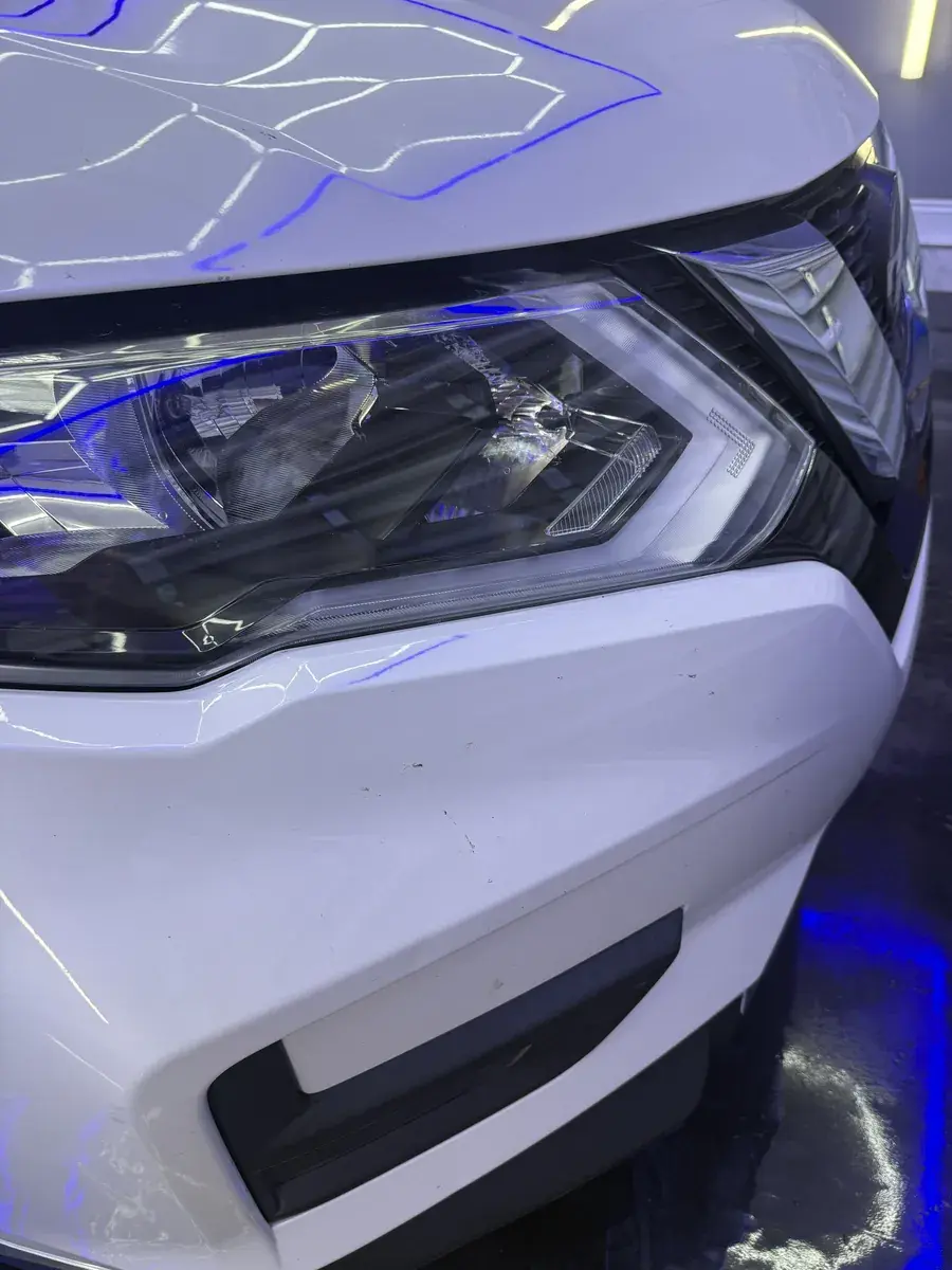 Headlight and front bumper of a white 2020 Nissan Rogue with bug spots during a full detail in Panama City FL