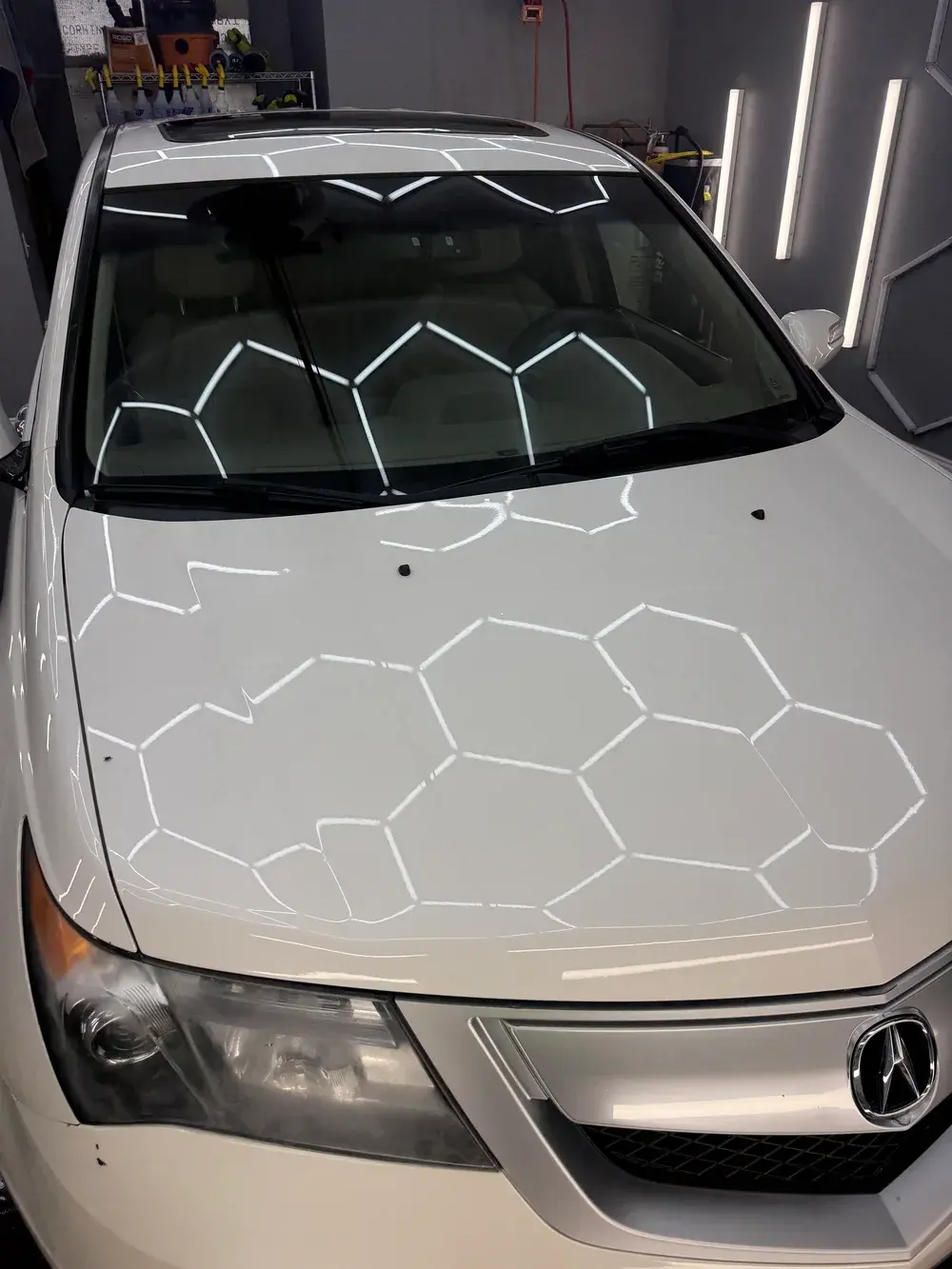 Hex shop lights reflected in the clean white hood of a 2011 Acura MDX after an exterior detail in Panama City FL