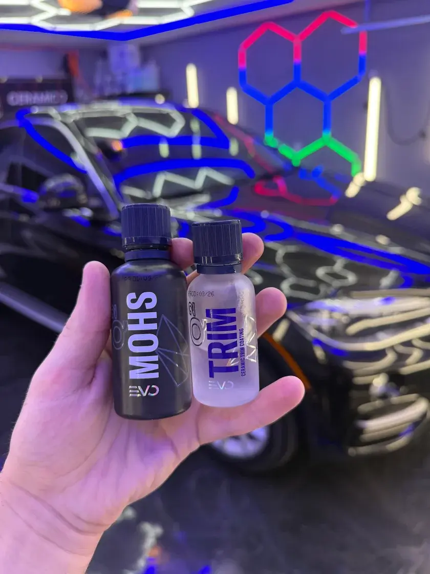 Gyeon Q2 Mohs EVO and Q2 Trim ceramic coating bottles held in front of a black 2016 BMW X6 at Ceramico in Panama City FL
