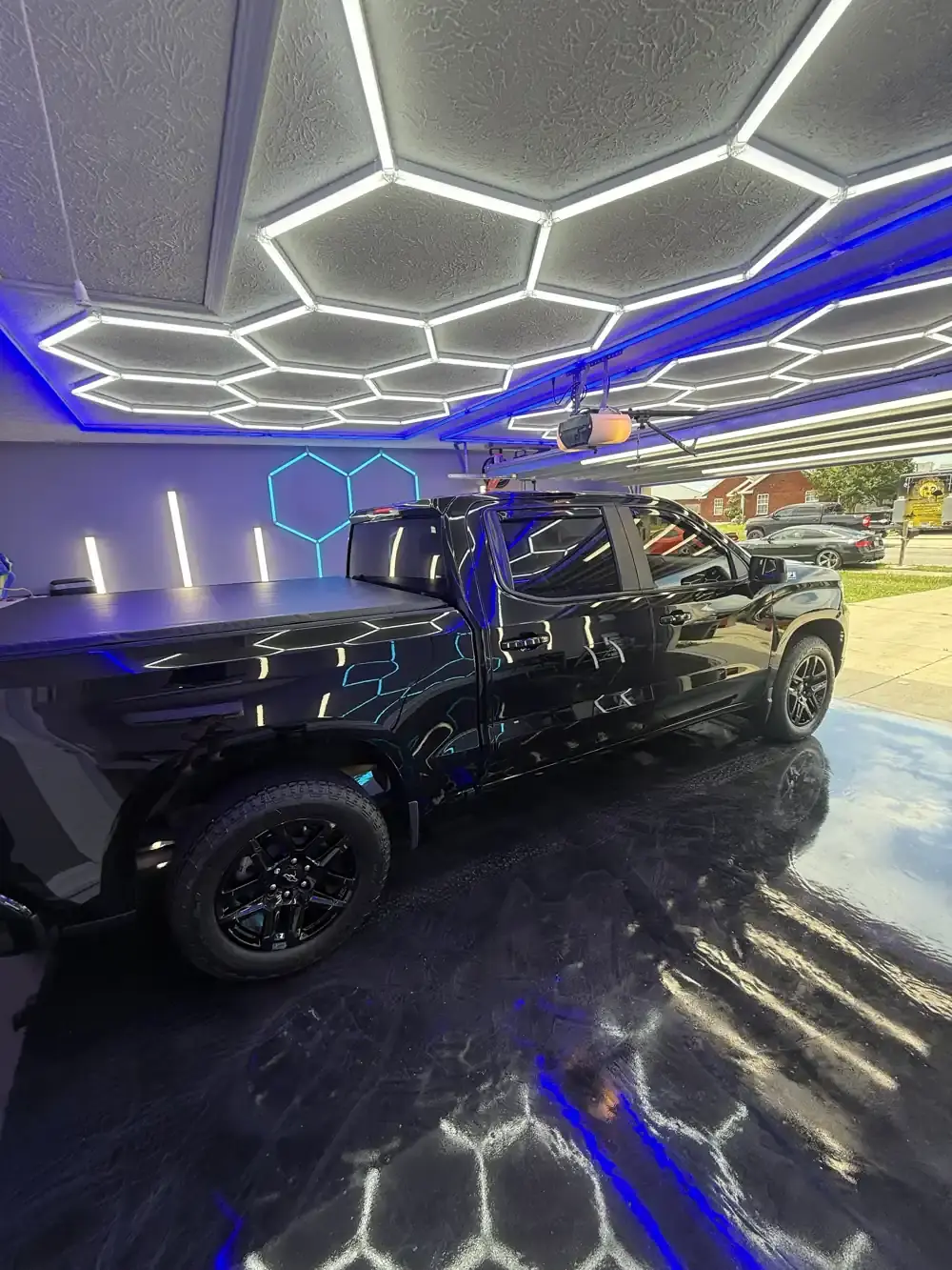 Rear three-quarter view of a ceramic coated black Chevy Silverado reflecting the hex shop lights in Panama City FL